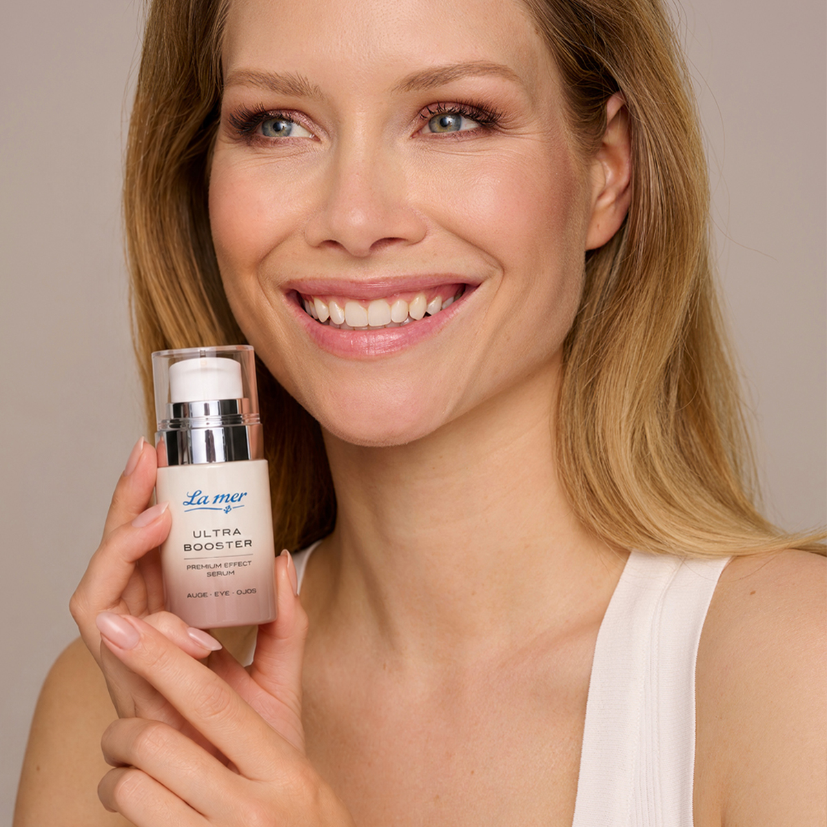 Lächelnde Frau hält das La mer Ultra Booster Premium Effect Serum. Augenpflege für eine frische, strahlende Augenpartie.