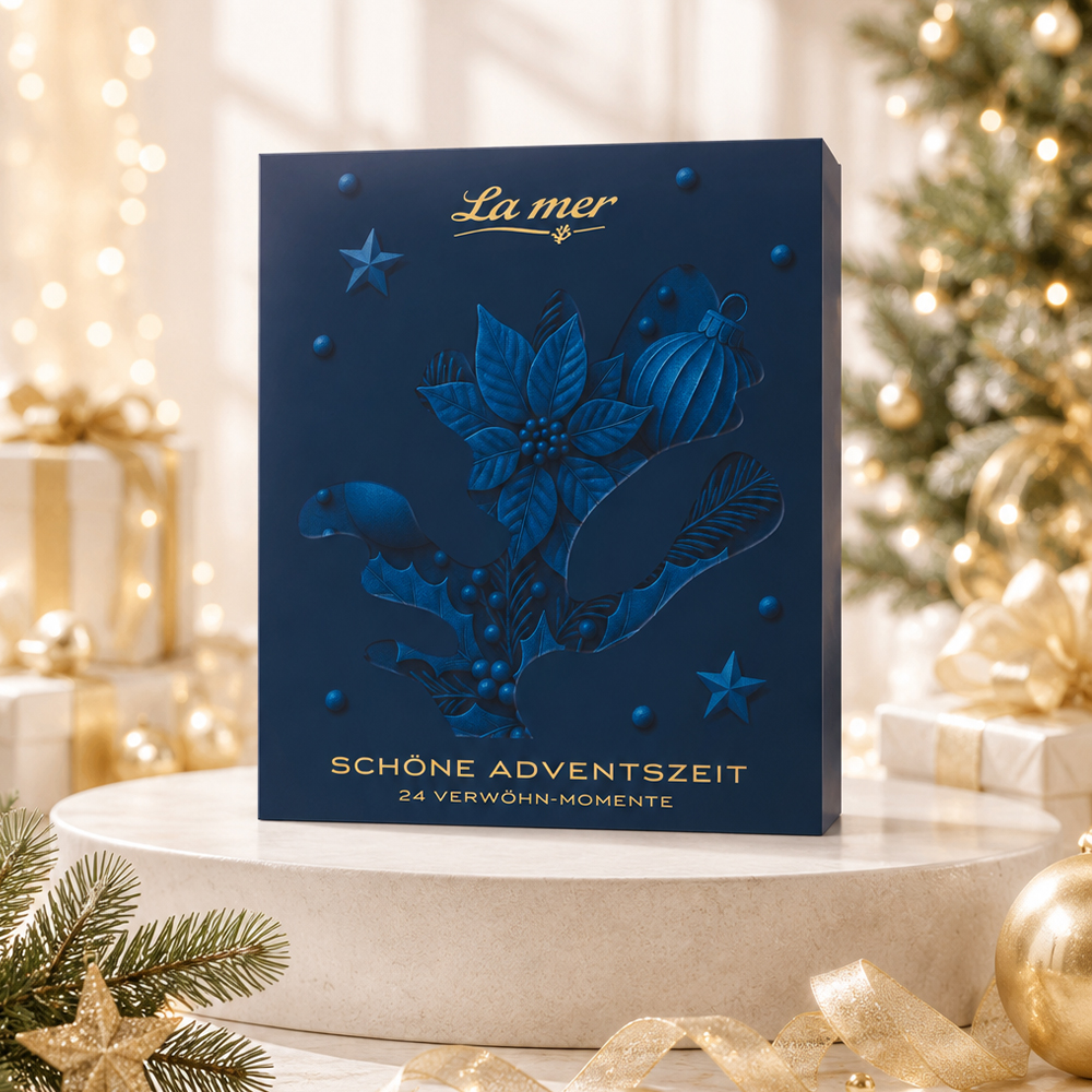 La mer Adventskalender in dunkelblau vor festlich geschmücktem Weihnachtsbaum mit Lichtern und Geschenken